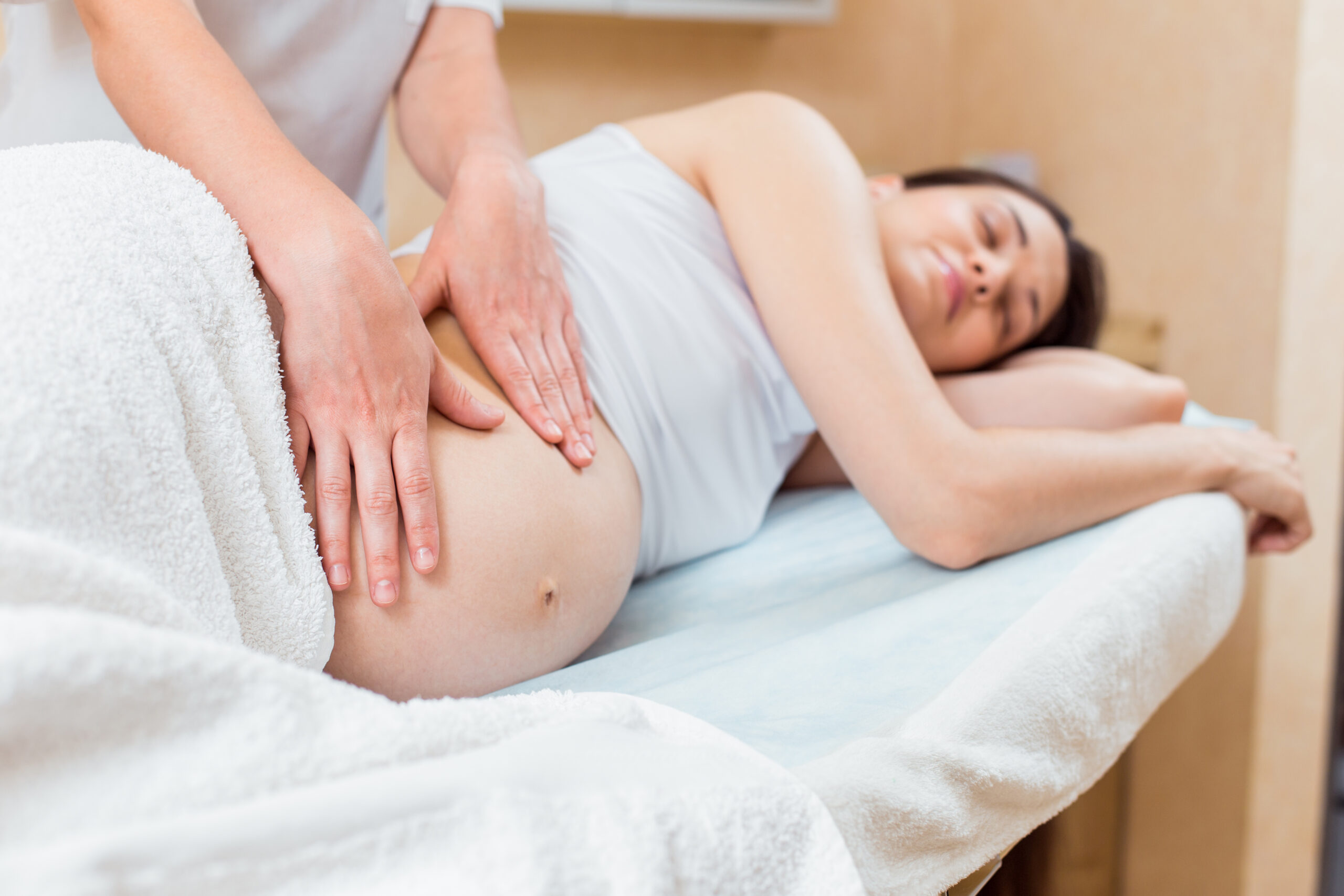 beautiful pregnant brunette with long hair lies her side reception with massage therapist cosmetology room scaled - Well-Being Massage