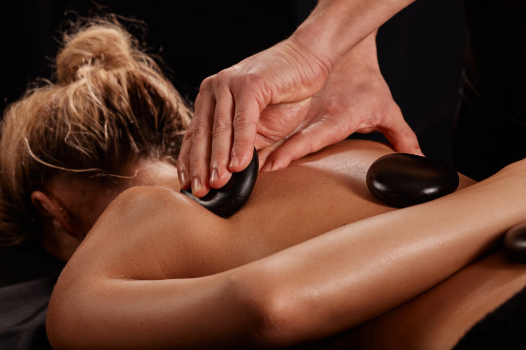 man receives hot stone massage masseur gives stone massage - Well-Being Massage